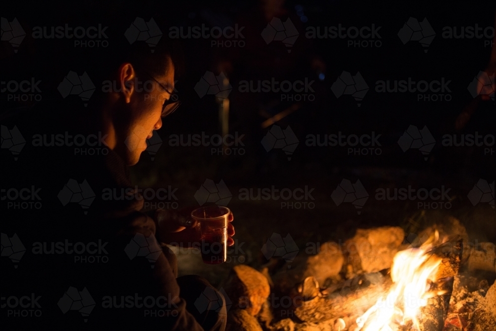 Man sits by a camp fire - Australian Stock Image