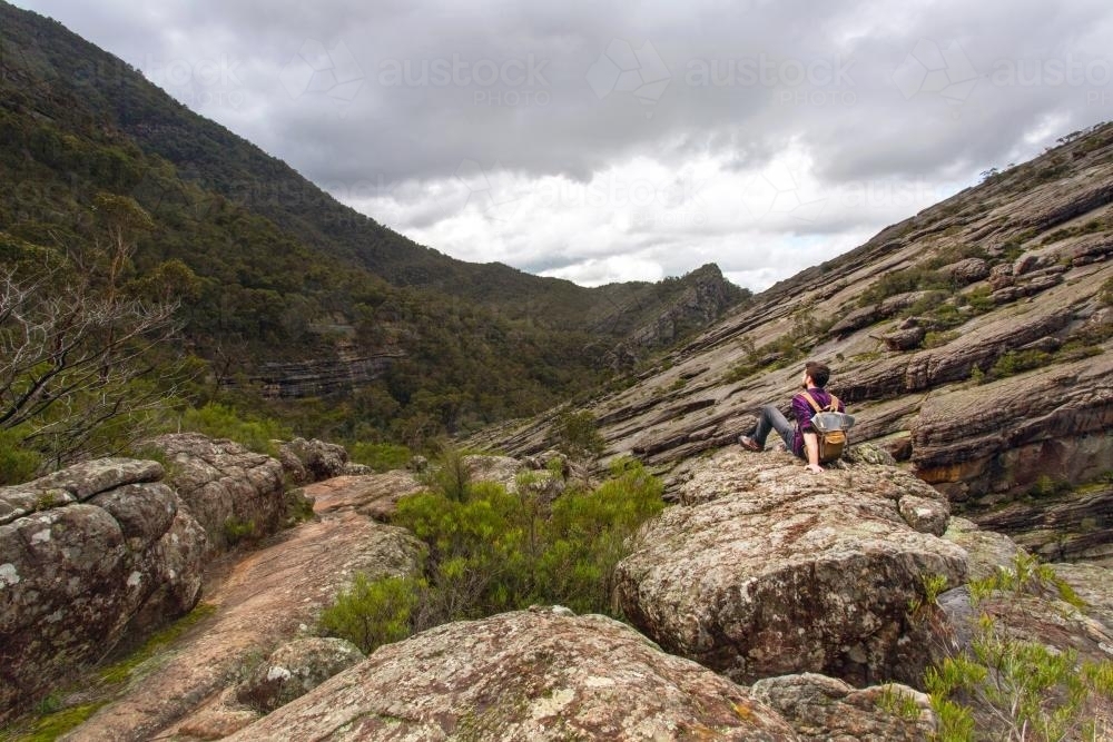 Man sitting alone in a large valley with overcast sky - Australian Stock Image