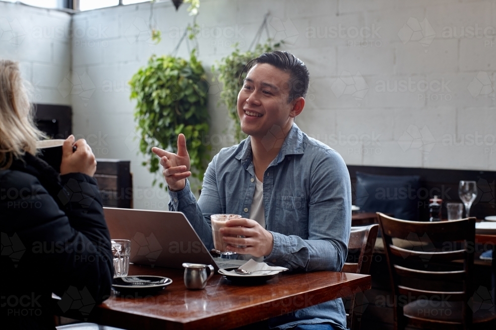 Man sitting at table at restaurant talking with friend - Australian Stock Image