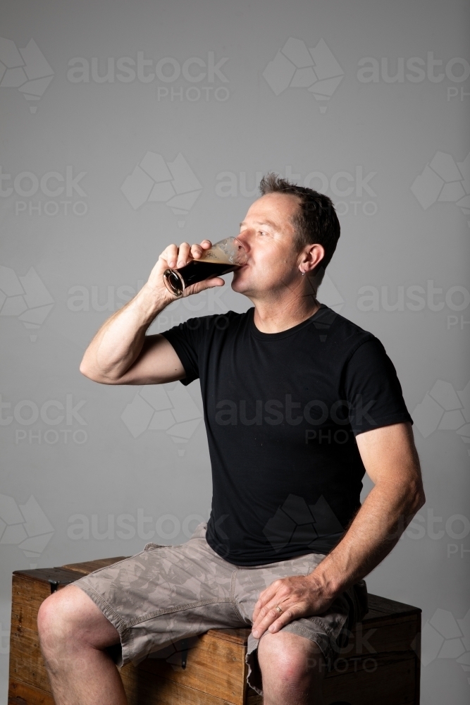 Man sitting, drinking a glass of beer, relaxed and happy - Australian Stock Image