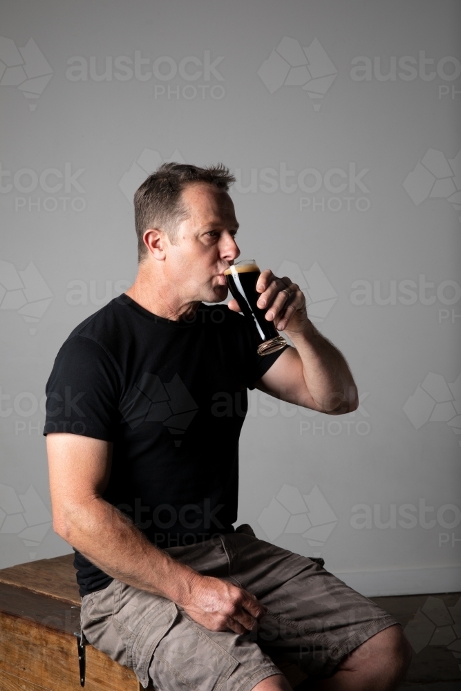 Man sitting, holding a glass of beer, relaxed and happy - Australian Stock Image