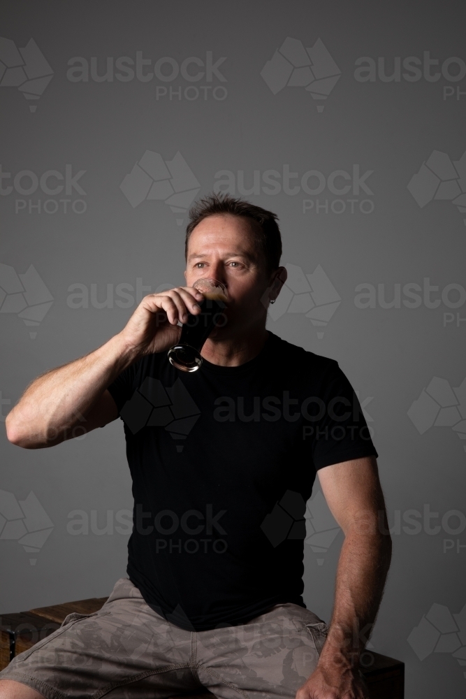 Man sitting, holding a glass of beer, relaxed and happy - Australian Stock Image