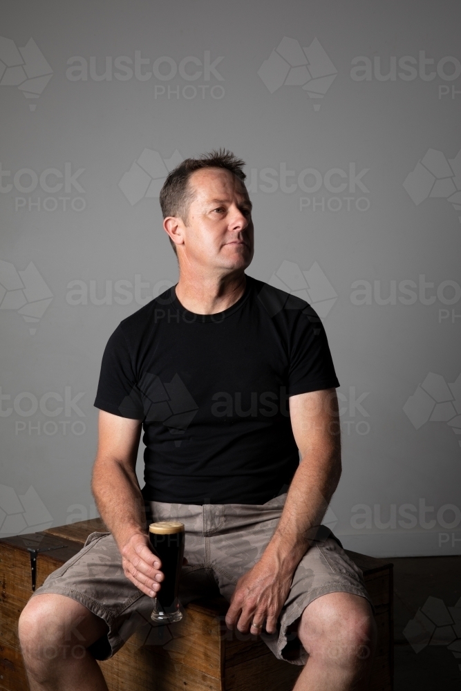 Man sitting, holding a glass of beer, relaxed and happy - Australian Stock Image