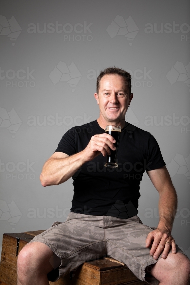 Man sitting, holding a glass of beer, relaxed and happy - Australian Stock Image