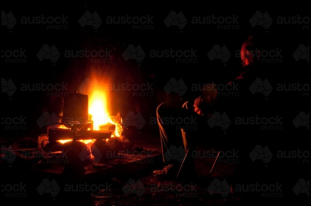 Man sitting in front of campfire boiling the billy at night - Australian Stock Image