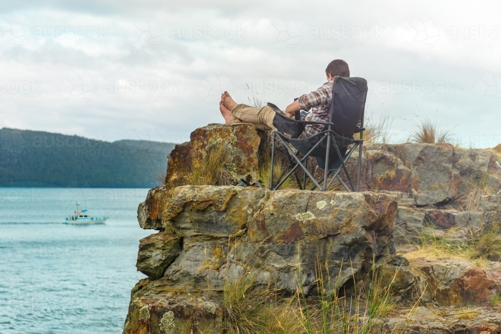 man sitting in tranquil camp spot by the ocean in his chair - Australian Stock Image