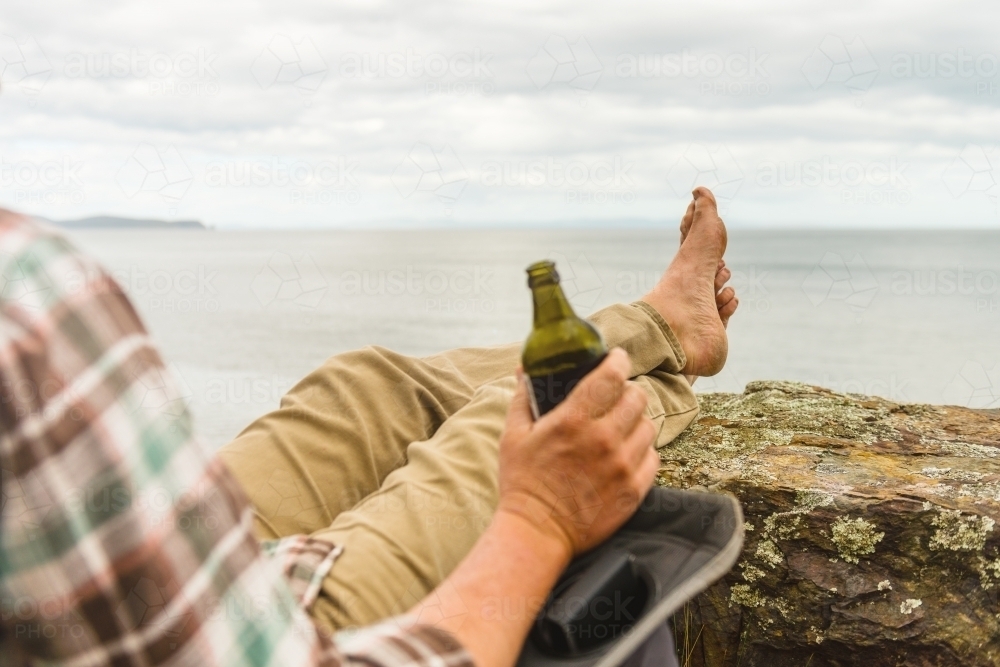 man sitting in tranquil camp spot by the ocean in his chair, with a beer - Australian Stock Image
