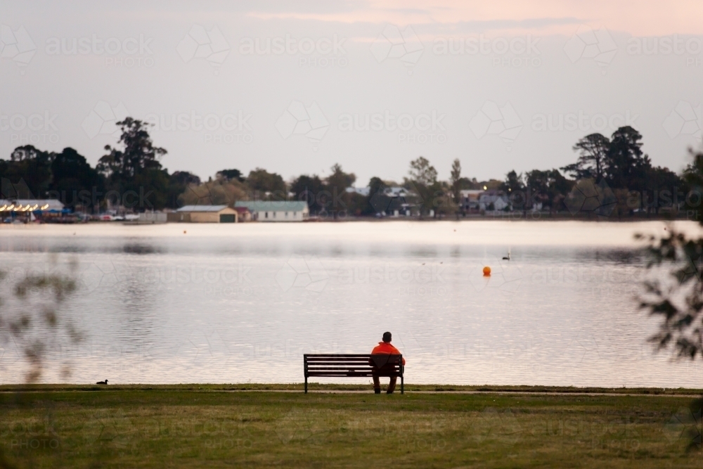 Man sitting on a bench seat at the lakeside - Australian Stock Image