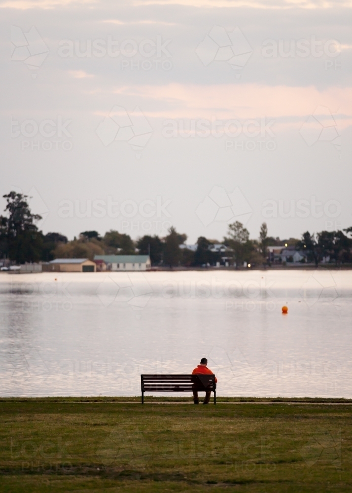 Man sitting on a bench seat at the lakeside - Australian Stock Image