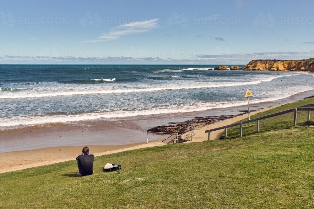 Man sitting on a grassy slope watching the surf - Australian Stock Image
