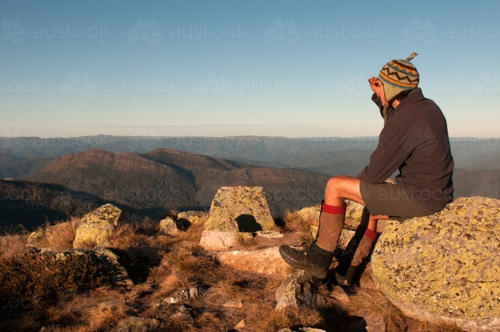 Man sitting on a rock looking out over mountain range - Australian Stock Image