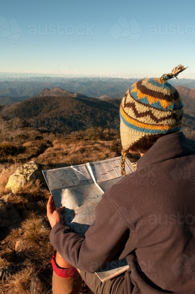 Man sitting on a rock overlooking mountain ranges, looking at a map. - Australian Stock Image