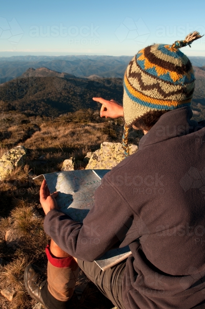 Man sitting on a rock overlooking mountain ranges, looking at a map - Australian Stock Image
