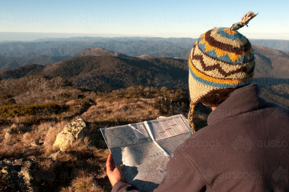 Man sitting on a rock overlooking mountain ranges, looking at a map - Australian Stock Image