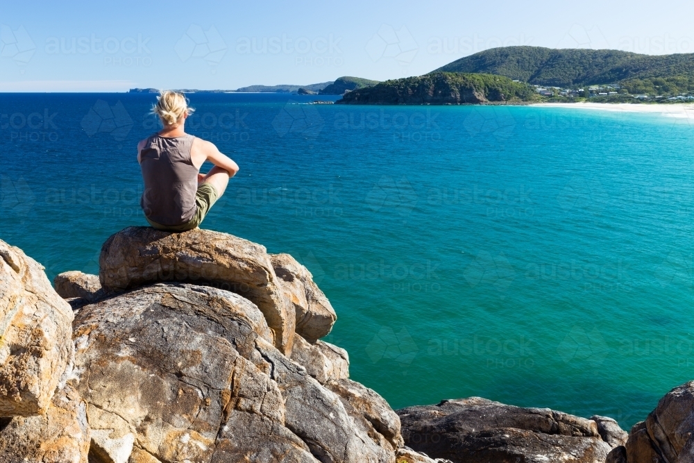 Man sitting on a rocky headland looking out to sea - Australian Stock Image