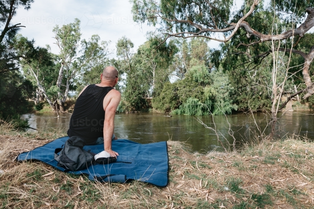 Man sitting on a rug next to a river in the bush : Austockphoto Man sitting on a rug next to a river in the bush - Australian Stock Image