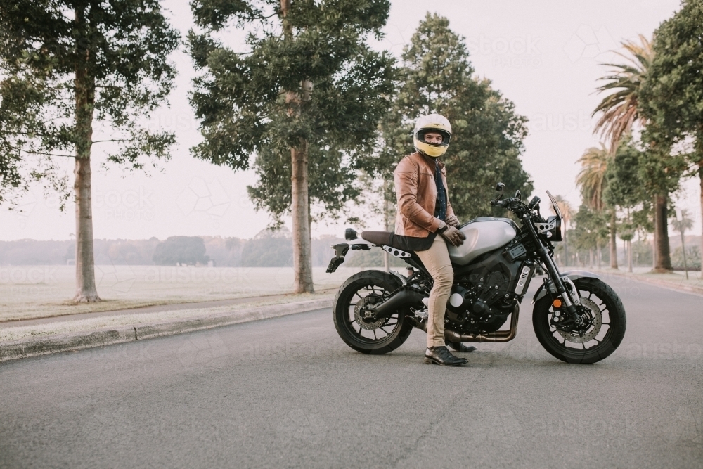 Man sitting on motorbike in middle of road at parklands - Australian Stock Image