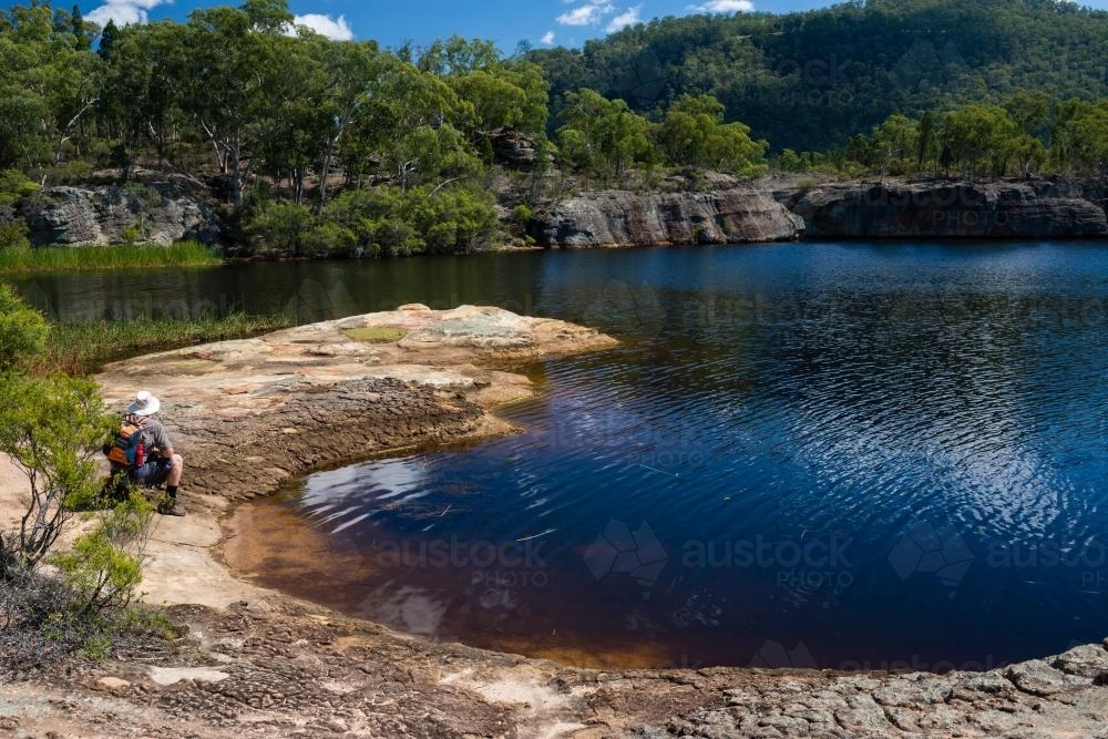 Man sitting on the banks of a waterway. - Australian Stock Image