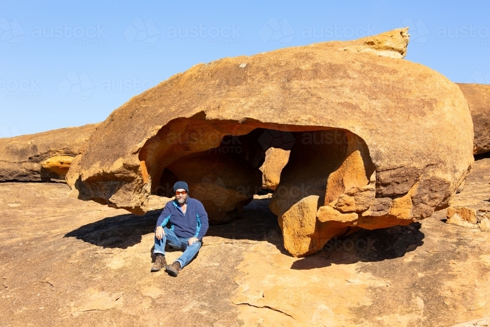 man sitting under granite rock formation in the Wheatbelt - Australian Stock Image