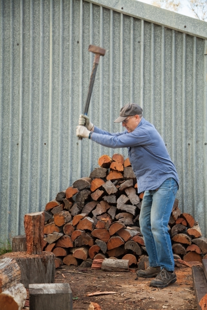 Man splitting logs of wood for fire in winter - Australian Stock Image