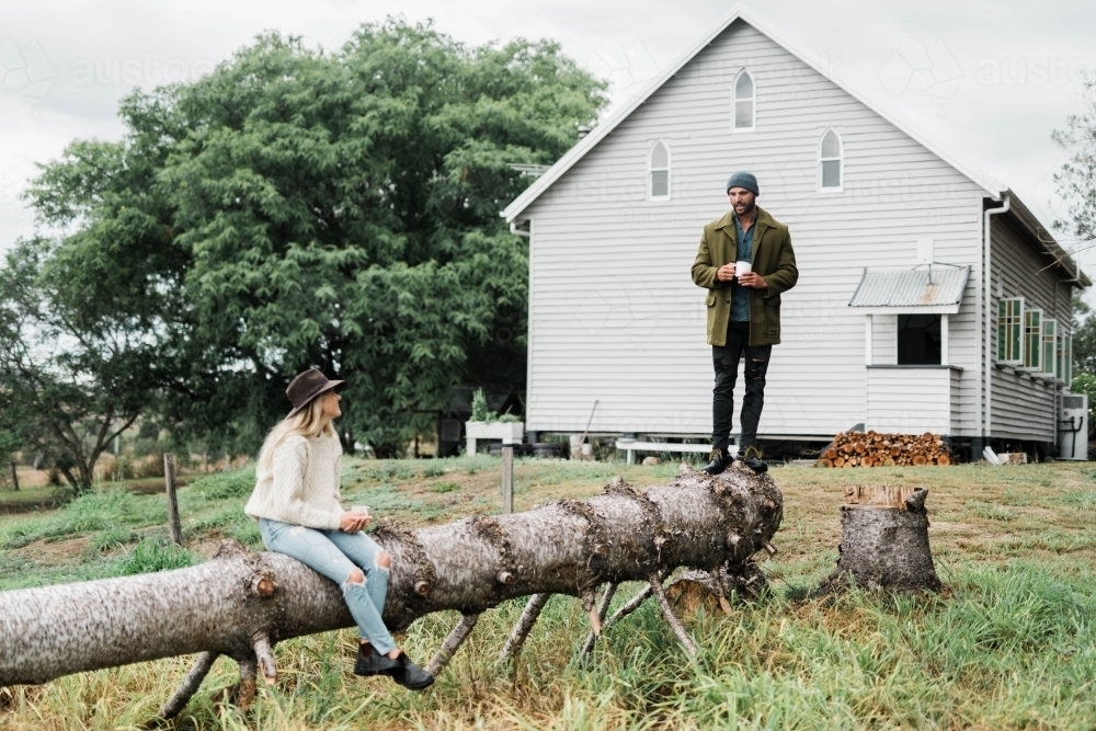 Man standing and woman sitting and drinking coffee on a fallen tree - Australian Stock Image