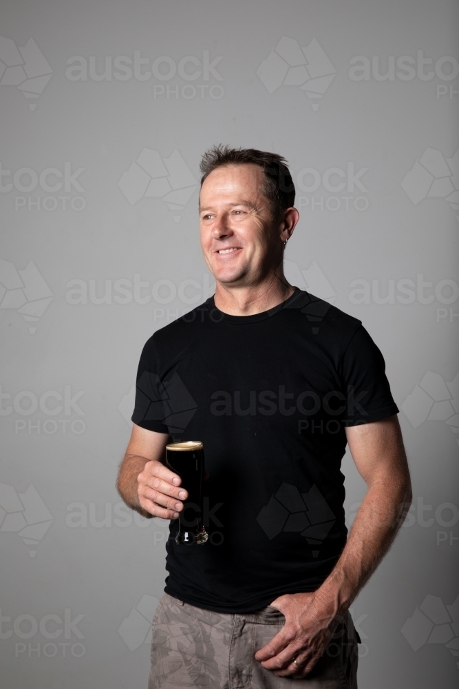 Man standing, holding a glass of beer, relaxed and happy - Australian Stock Image