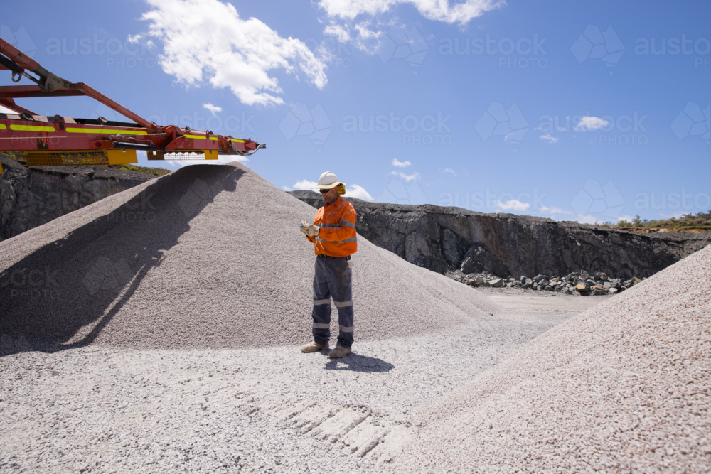 Man standing in between piles of aggregates near the crusher. - Australian Stock Image