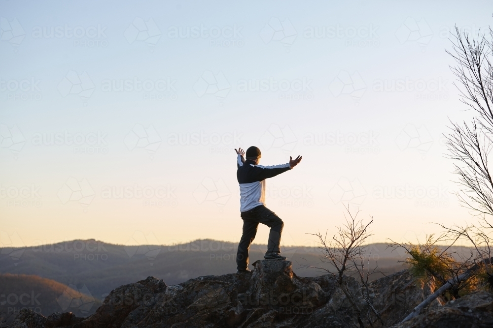 Man standing looking out over mountains on sunset - Australian Stock Image