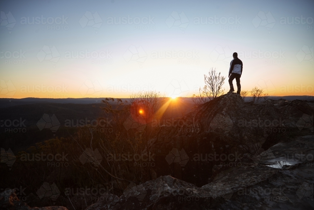 Man standing looking out over mountains on sunset - Australian Stock Image