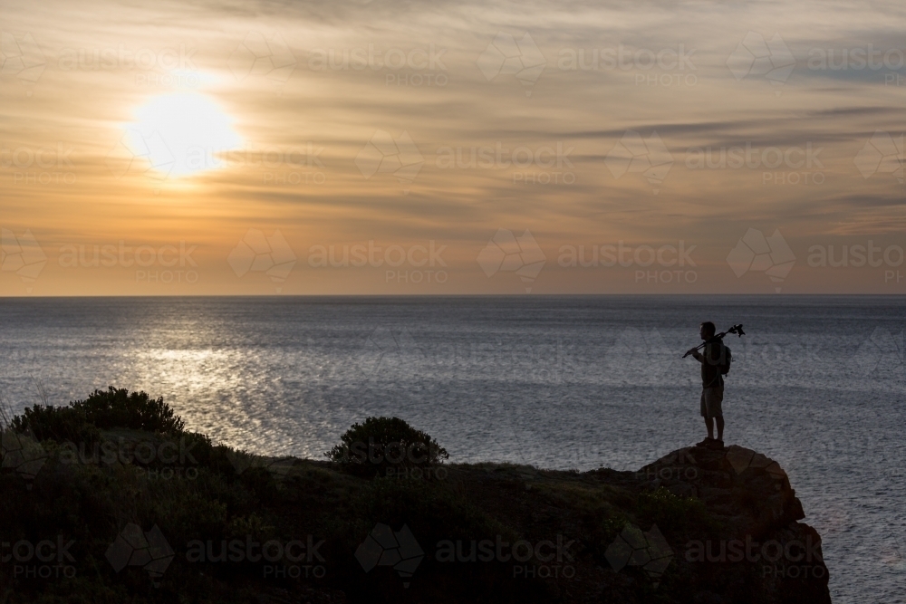 Man standing on headland at sunrise looking out over ocean - Australian Stock Image