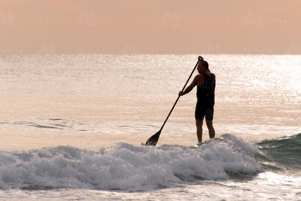 Man standing on paddleboard in pink dawn light - Australian Stock Image