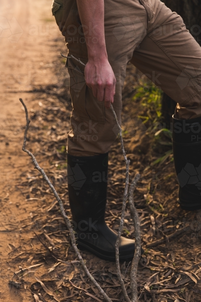 Man standing on side of rural dirt road, collecting wood for camp fire - Australian Stock Image