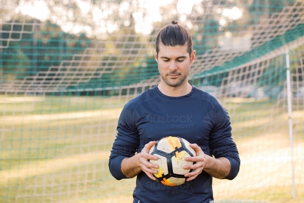 man standing on the field while looking down holding a soccer ball - Australian Stock Image