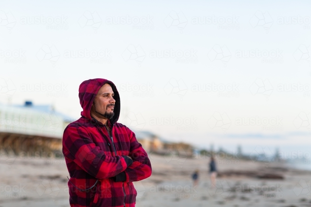 Man standing outdoors with arms crossed wearing red checked hoody - Australian Stock Image