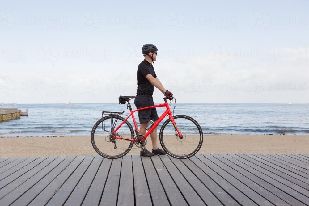 Man standing with bike looking at view of a Melbourne beach - Australian Stock Image