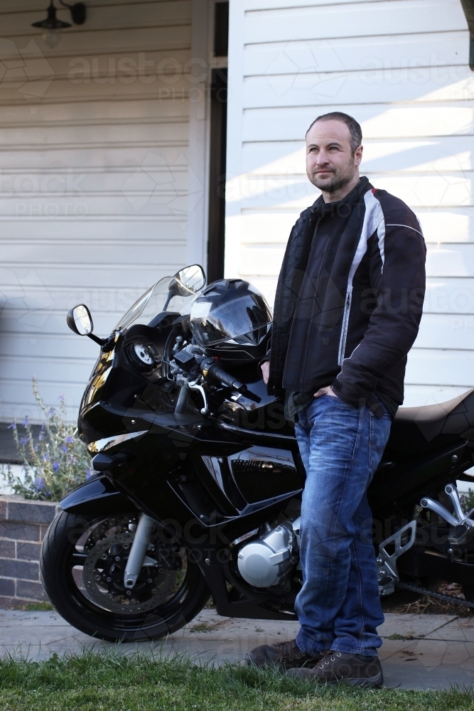 Man standing with motorbike outside of house - Australian Stock Image