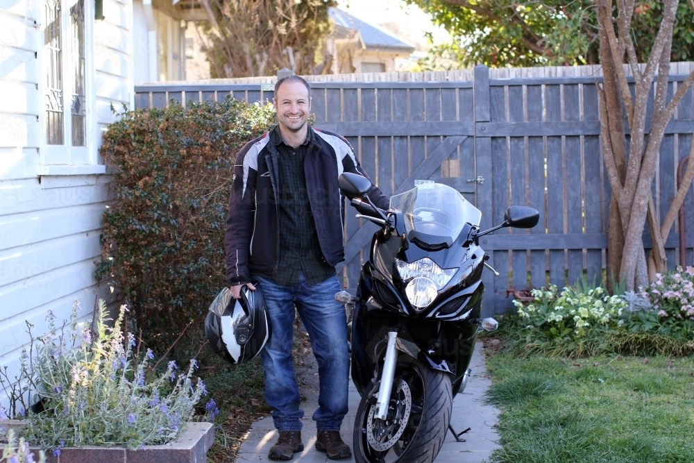 Man standing with motorbike outside of house - Australian Stock Image