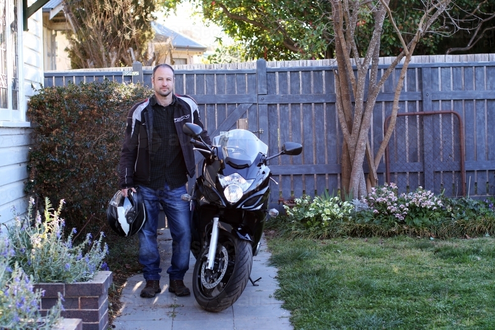 Man standing with motorcycle in front of garden fence - Australian Stock Image