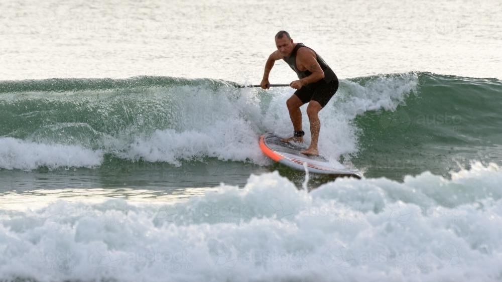 Man steering  paddleboard through wave - Australian Stock Image