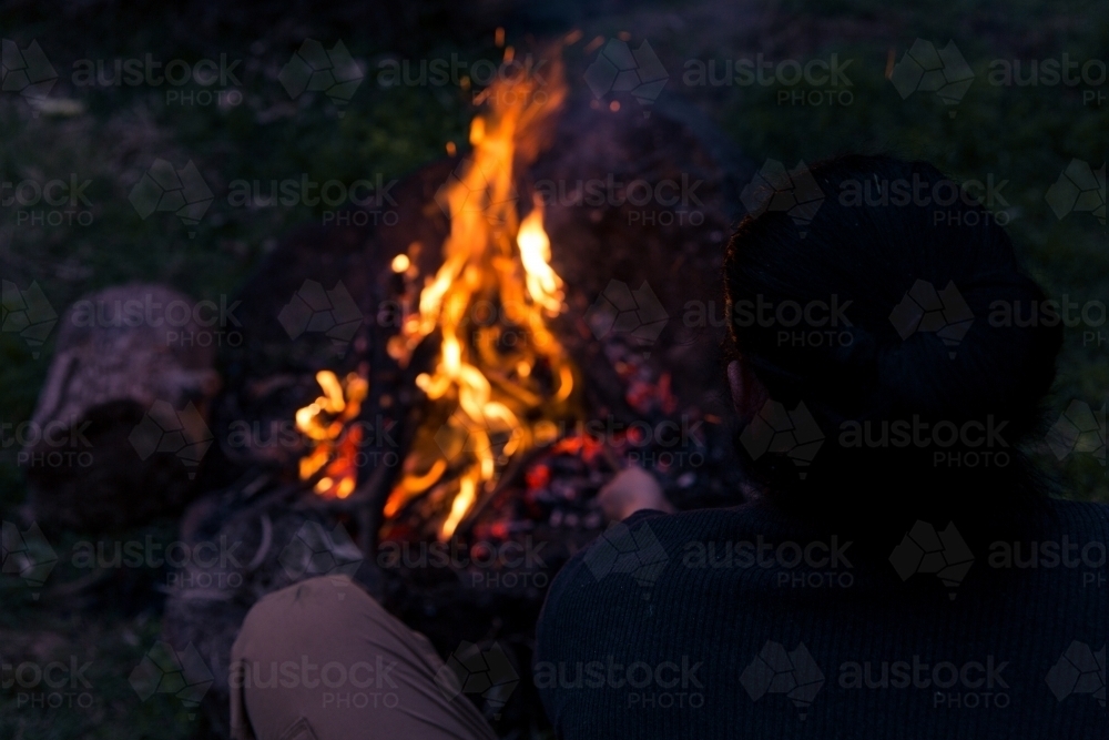Man stoking roaring camp fire at night - Australian Stock Image