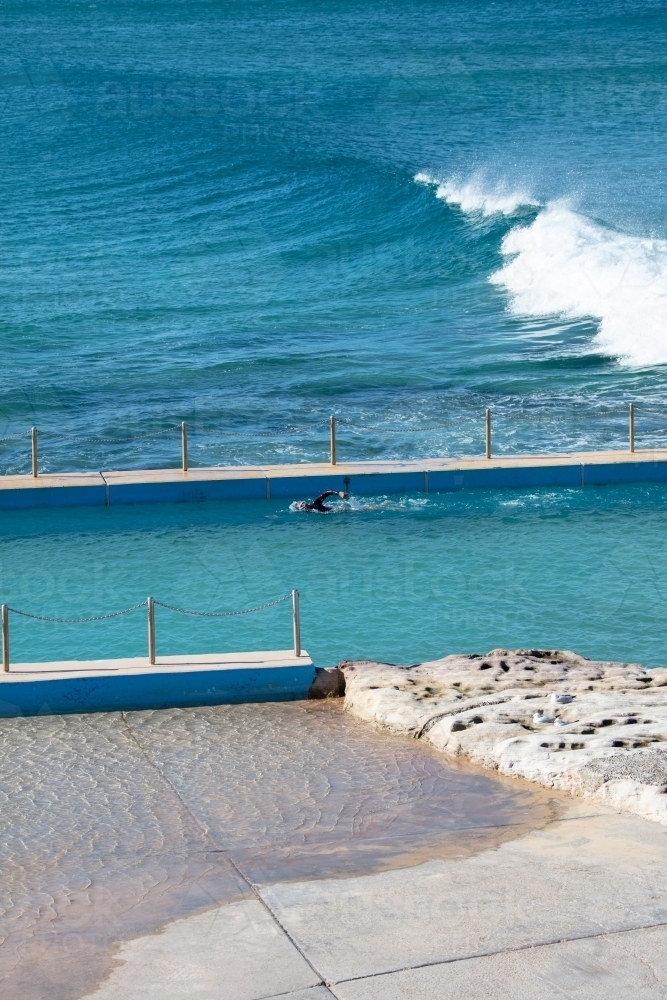 Man swimming in sea pool with wave behind - Australian Stock Image