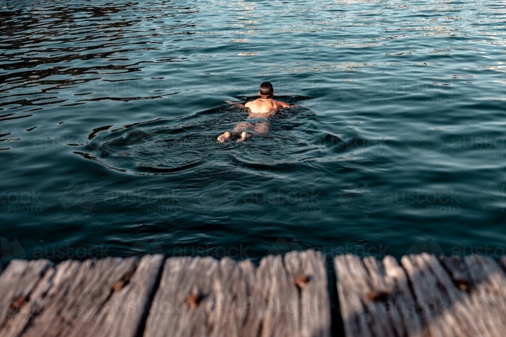Man swimming in the ocean near pier - Australian Stock Image