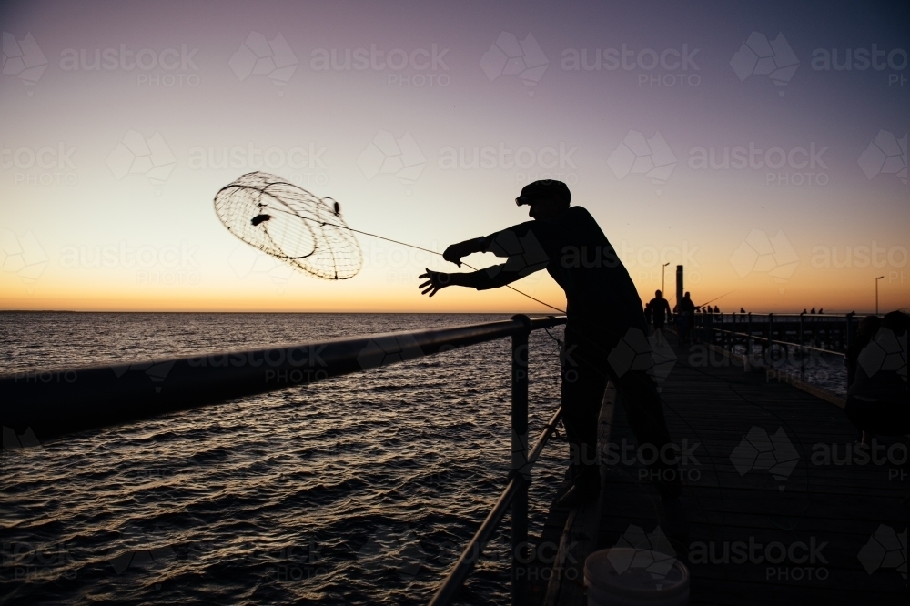 Man throwing crab pot at sunset - Australian Stock Image