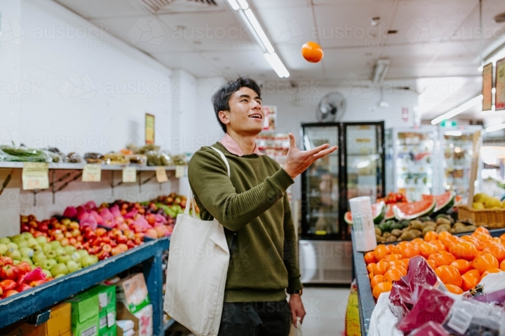 Man throwing up and catching mandarin in supermarket - Australian Stock Image