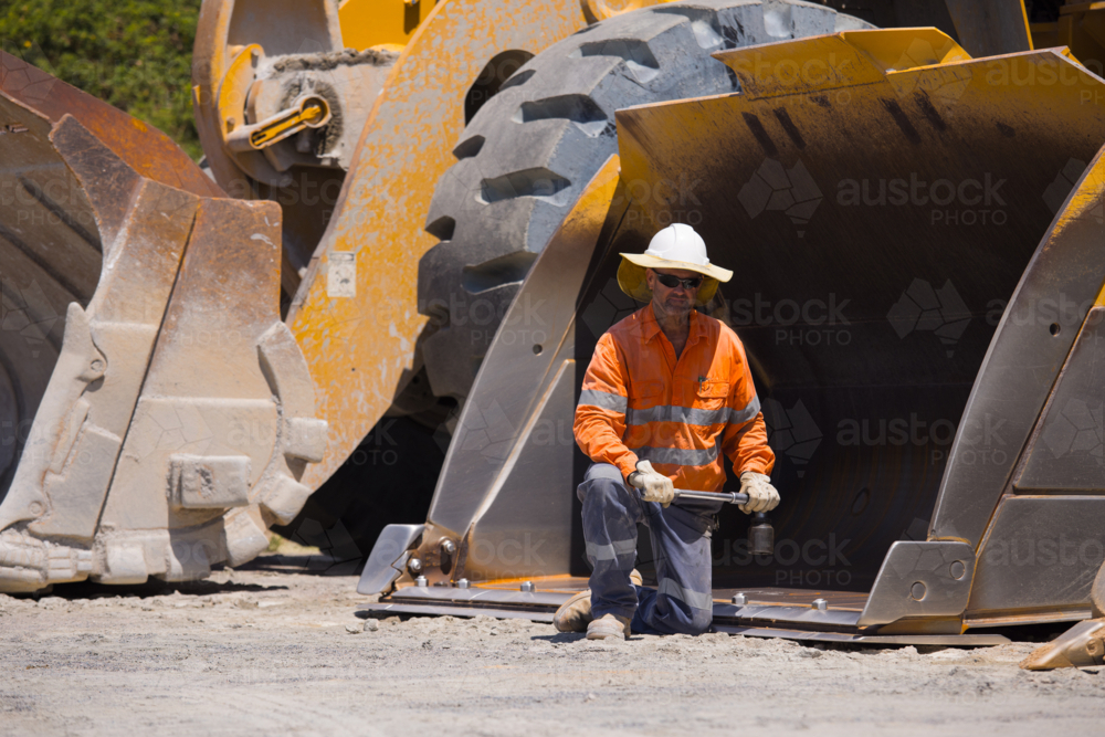 Man tightening the bolts on the bucket of a payloader. - Australian Stock Image