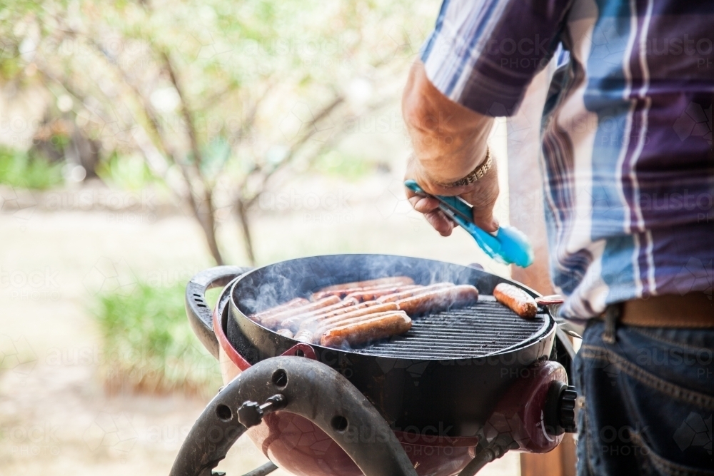 Man turning snags on a backyard barbie - Australian Stock Image