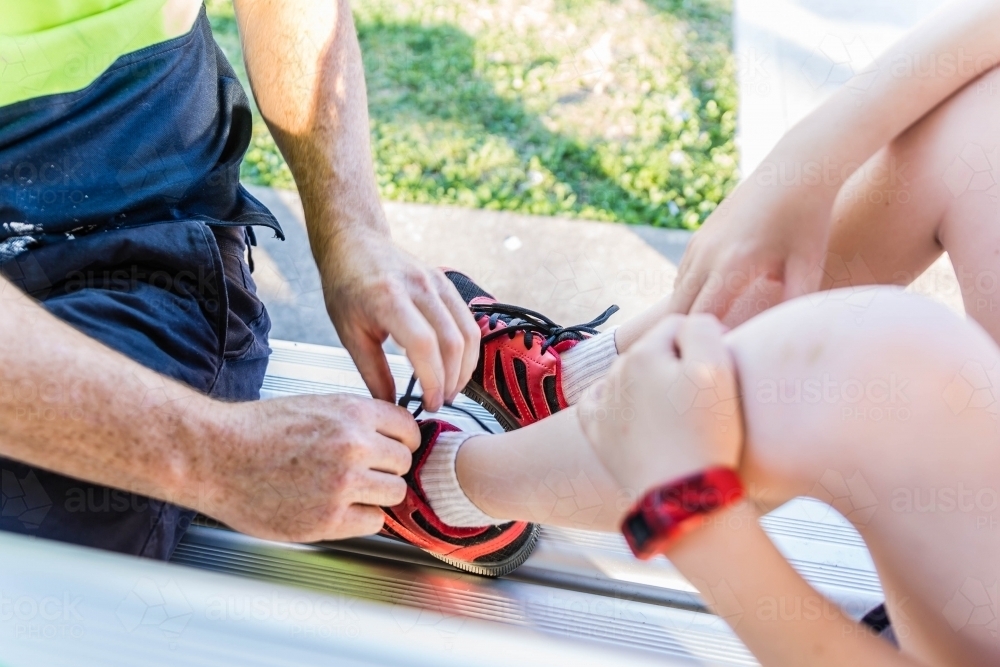 Man tying shoelaces on shoes of child - Australian Stock Image