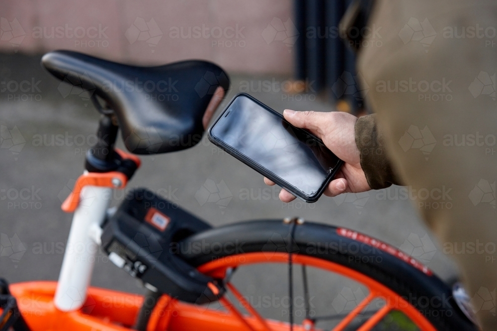 Man using mobile phone to unlock two-wheeled bike-sharing vehicle in city - Australian Stock Image