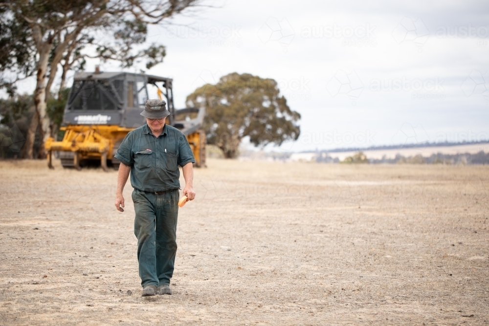man walking across dry ground away from bulldozer - Australian Stock Image