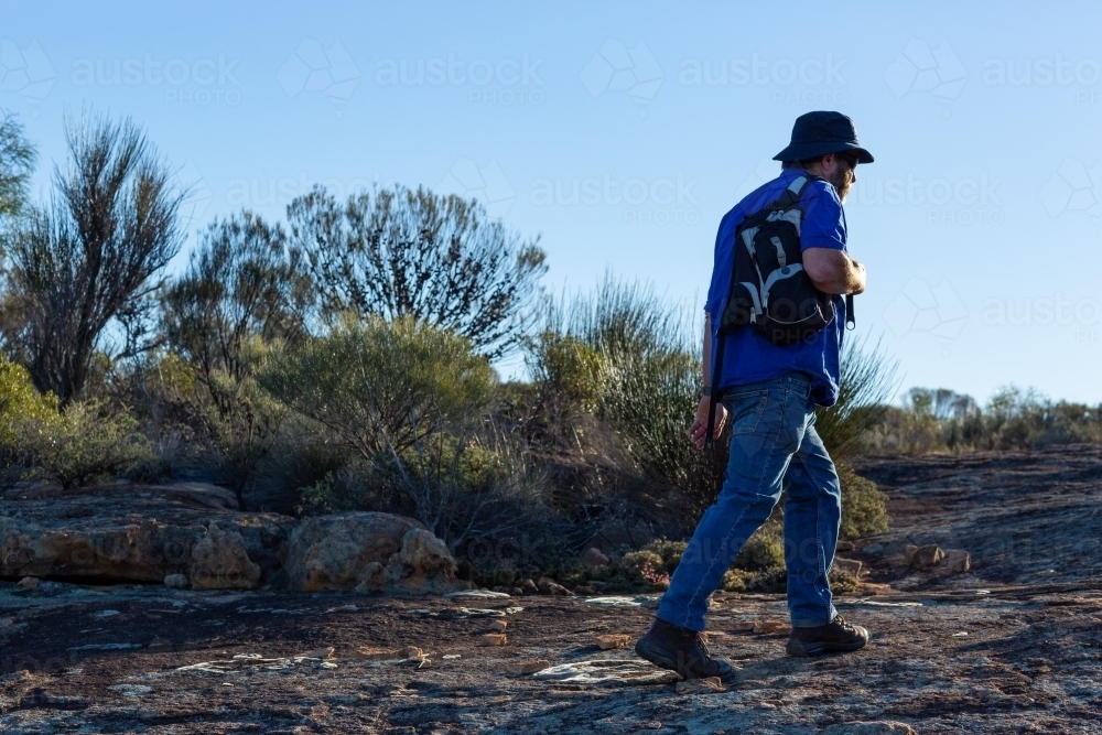 man walking across granite rock in the late afternoon light - Australian Stock Image